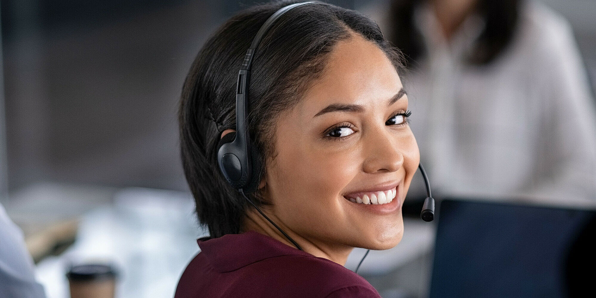 Portrait of smiling young businesswoman wearing headset in office. Portrait of a customer service agent looking at camera. Happy telephone operator latin girl with headset working at computer.